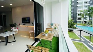 Un apartamento moderno con balcón, televisor en la sala y piscina al fondo.