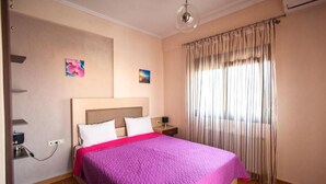 A hotel room with a bed, a nightstand, a lamp, and a window with curtains. - Amalia Lux Villas (Volvi)