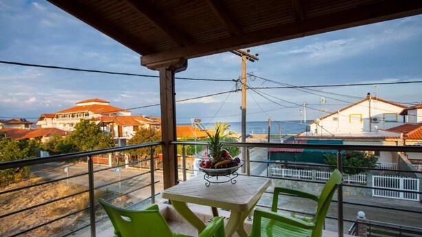 A balcony with a table and chairs, overlooking a coastal area with buildings and a clear sky. - Amalia Lux Villas (Volvi)