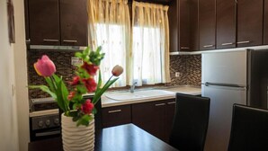 A modern kitchen with dark wooden cabinets, a stainless steel refrigerator, a brick backsplash, and a window with sheer curtains. - Amalia Lux Villas (Volvi)