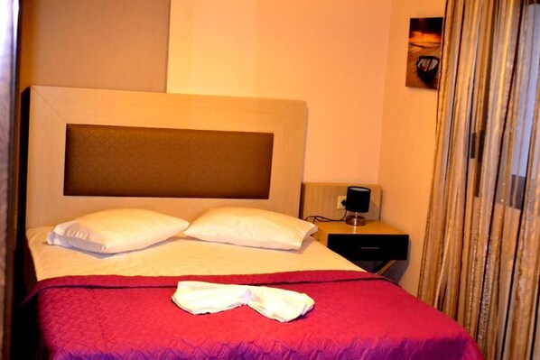 Une chambre d’hôtel avec un grand lit, deux oreillers, une couverture rouge, une serviette blanche, une table de chevet avec une lampe et un tableau au mur.