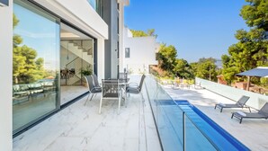 En modern uteplats med glasräcke, en pool och solstolar.