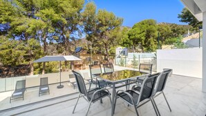 Une terrasse avec une table et des chaises en verre, entourée d’arbres et sous un ciel dégagé.