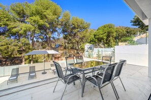 Una terraza con mesa y sillas de vidrio, rodeada de árboles y un cielo despejado.