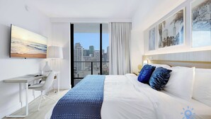 Hotellihuone, jossa on sänky, työpöytä, tuoli ja suuri ikkuna, josta on näkymä kaupunkiin.