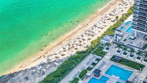 Vue aérienne d’un complexe hôtelier de bord de mer, avec une piscine, des parasols et un bâtiment d’hôtel.
