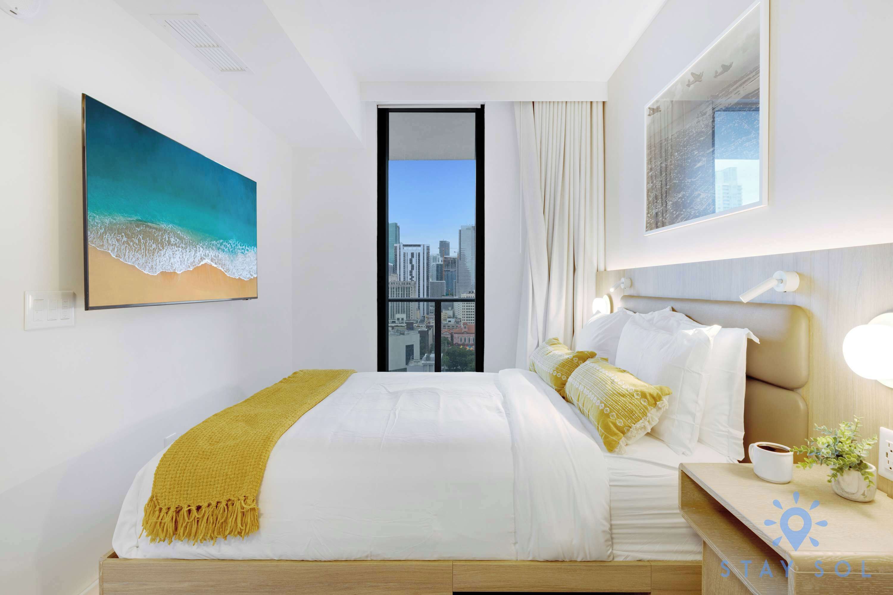 Een moderne hotelkamer met een groot bed, uitzicht over de stad en een schilderij van een strand.
