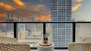 A high-rise hotel room with a city view, a round table with bottles and glasses, and wicker chairs. - Stylish 2BR with Pool & Balcony (Miami)
