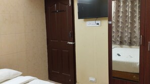 Un dormitori amb un llit, una televisió penjada a la paret, un armari i una porta.