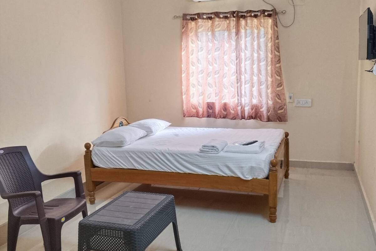 Une chambre avec un lit simple, un ventilateur de plafond, un appareil de climatisation, une chaise et une petite table.