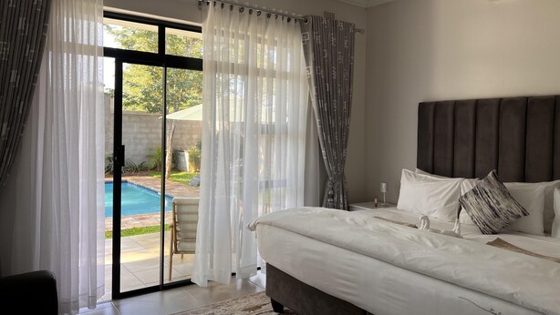 Un dormitorio con una cama grande, cabecera y vista a una piscina a través de un ventanal.