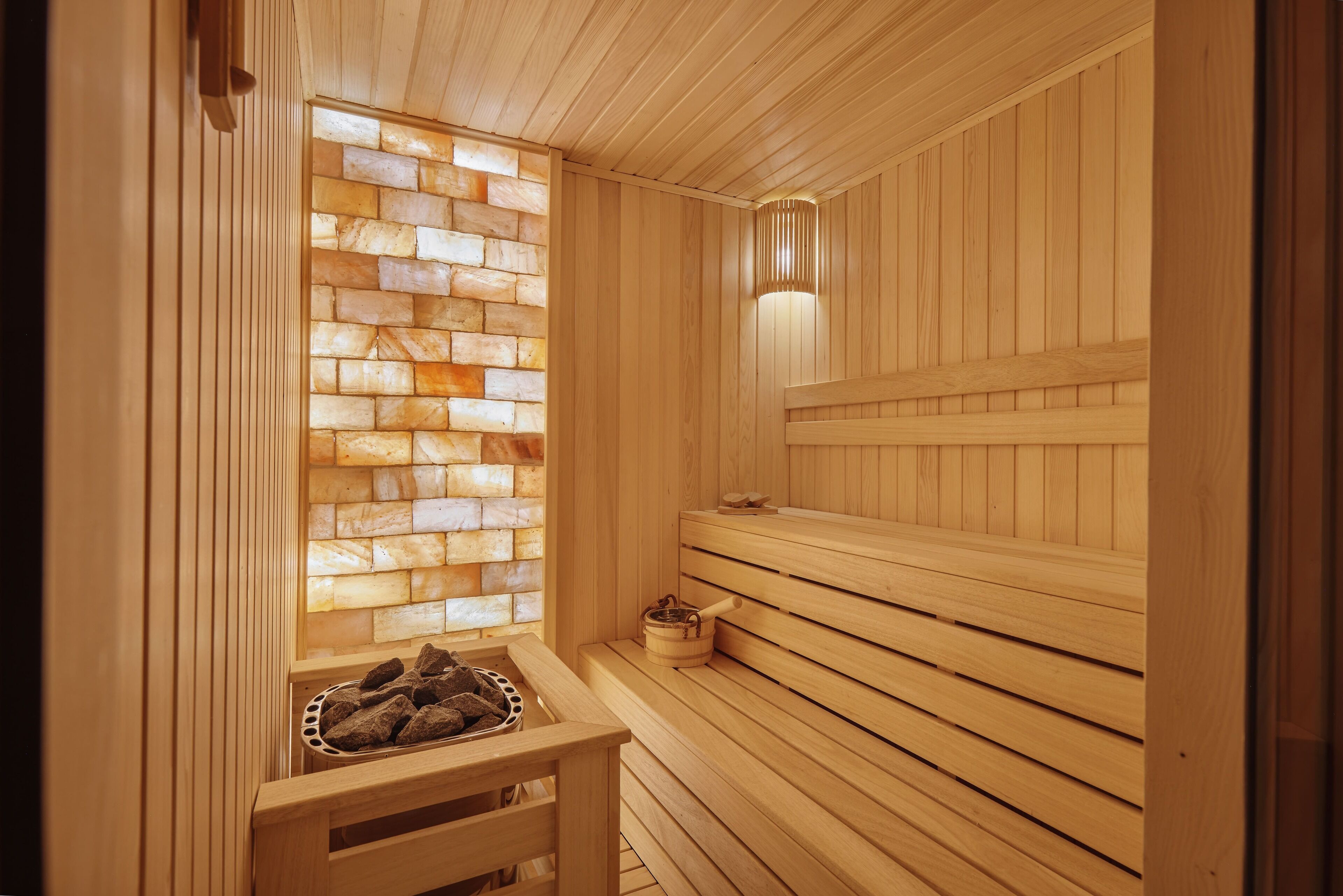A wooden sauna with a stone wall and benches.