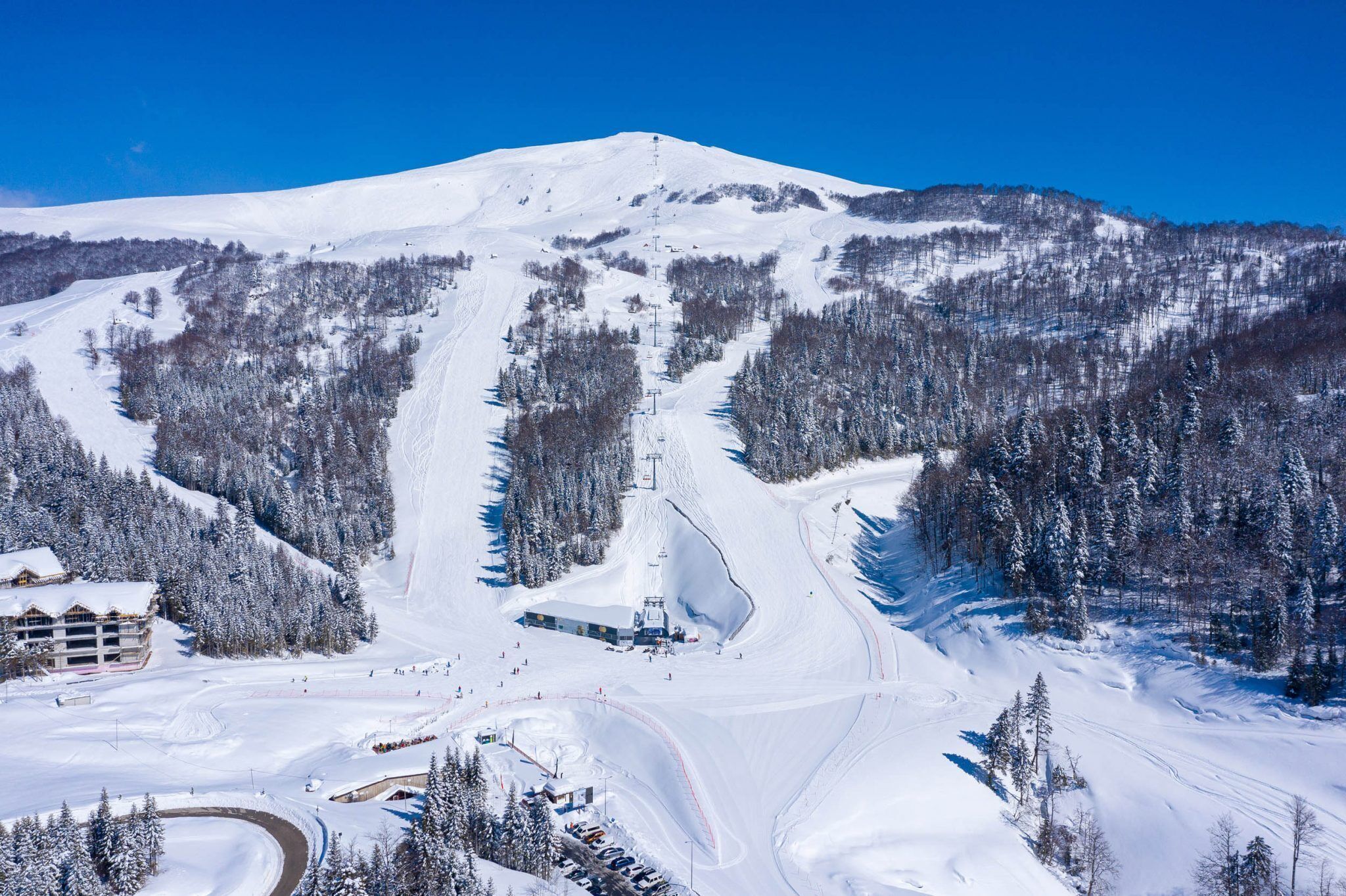 Estación de esquí nevada con telesilla, pistas y una cabaña.