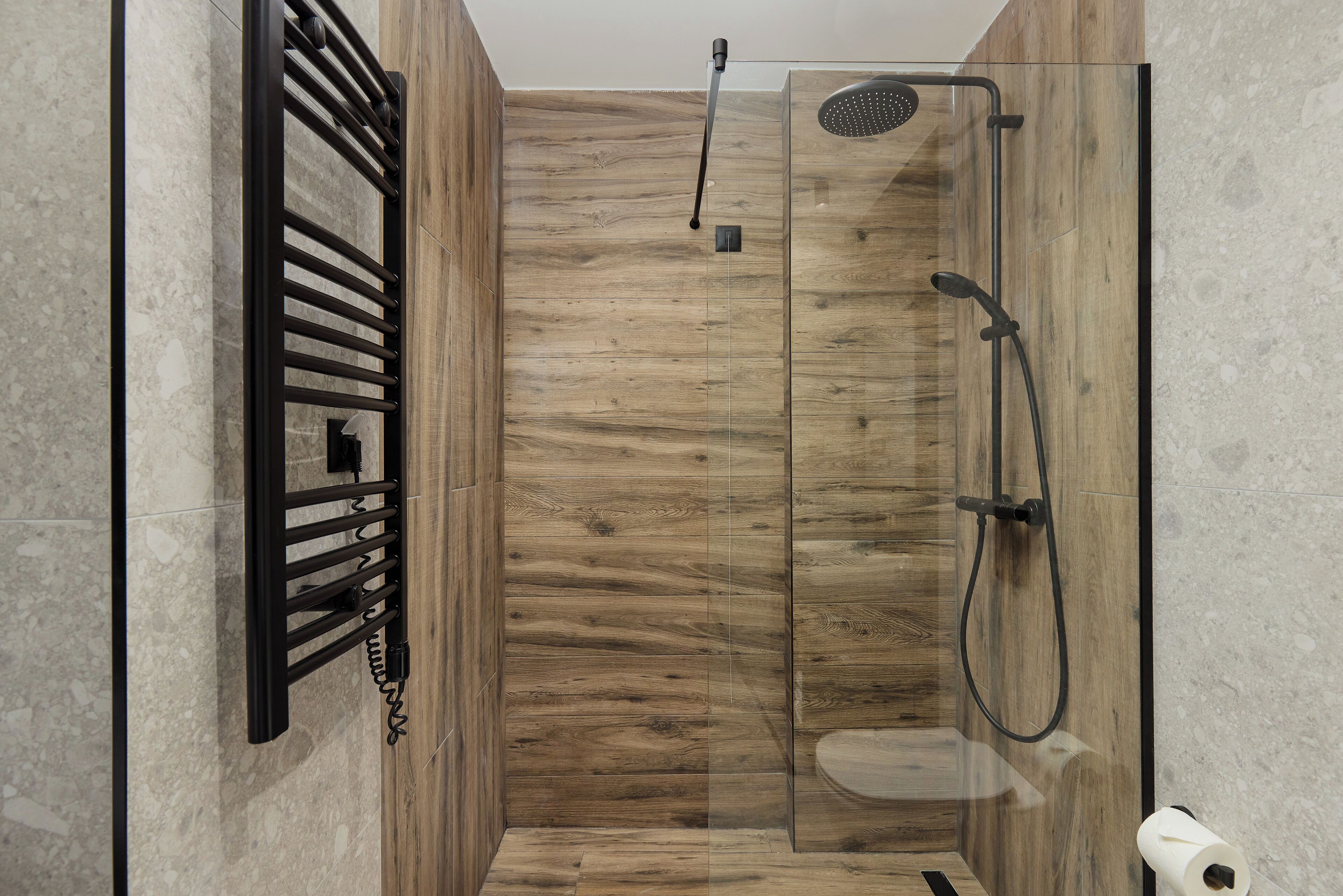 Una ducha moderna con cerramiento de vidrio, pared de paneles de madera y un perchero negro.