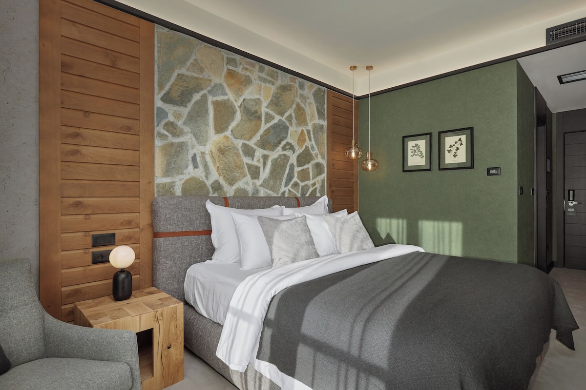 A modern bedroom with a stone accent wall, a wooden headboard, and a bedside table with a lamp.