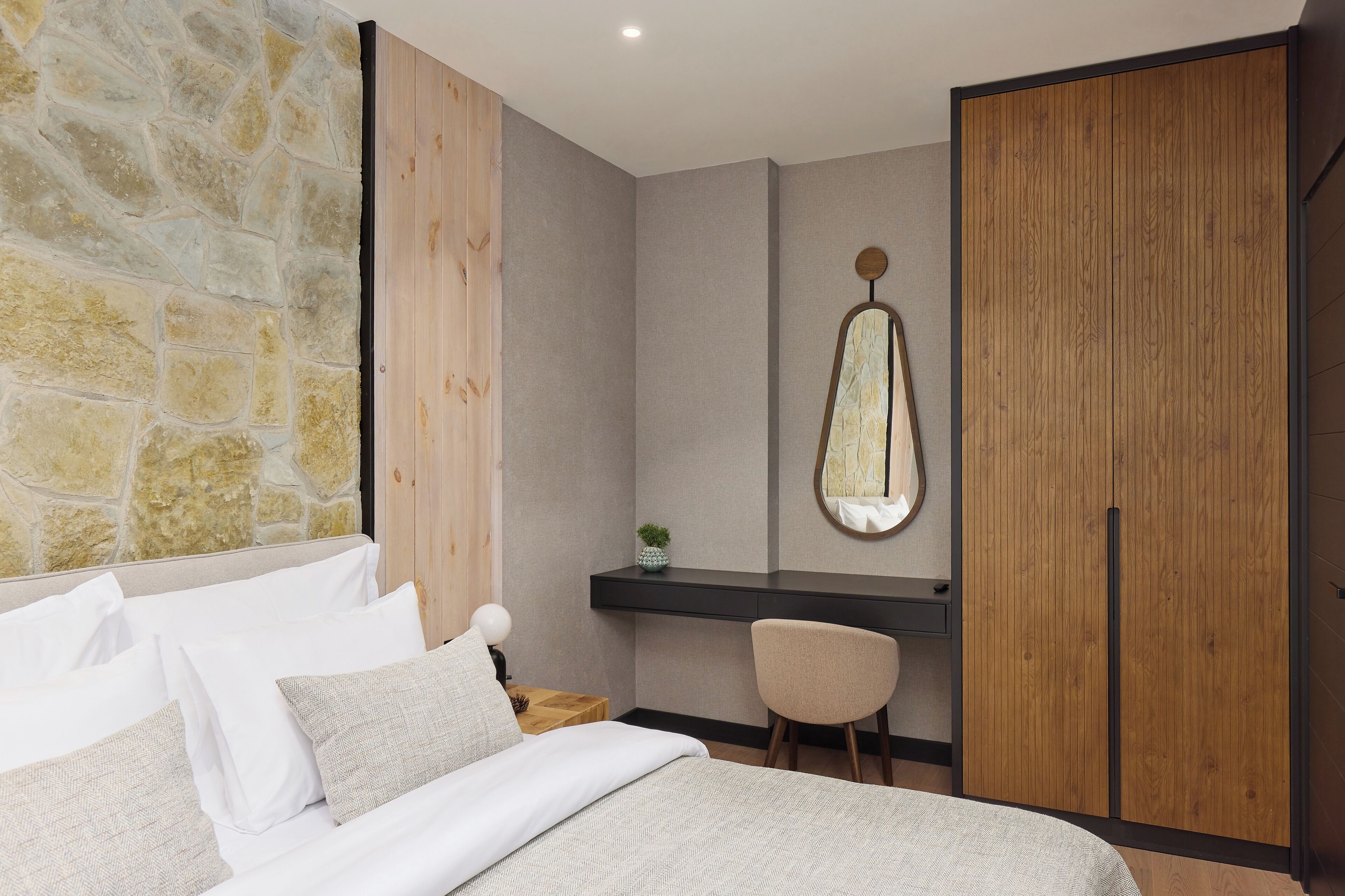 Un dormitorio con pared de piedra, un armario de madera, un escritorio y una silla.