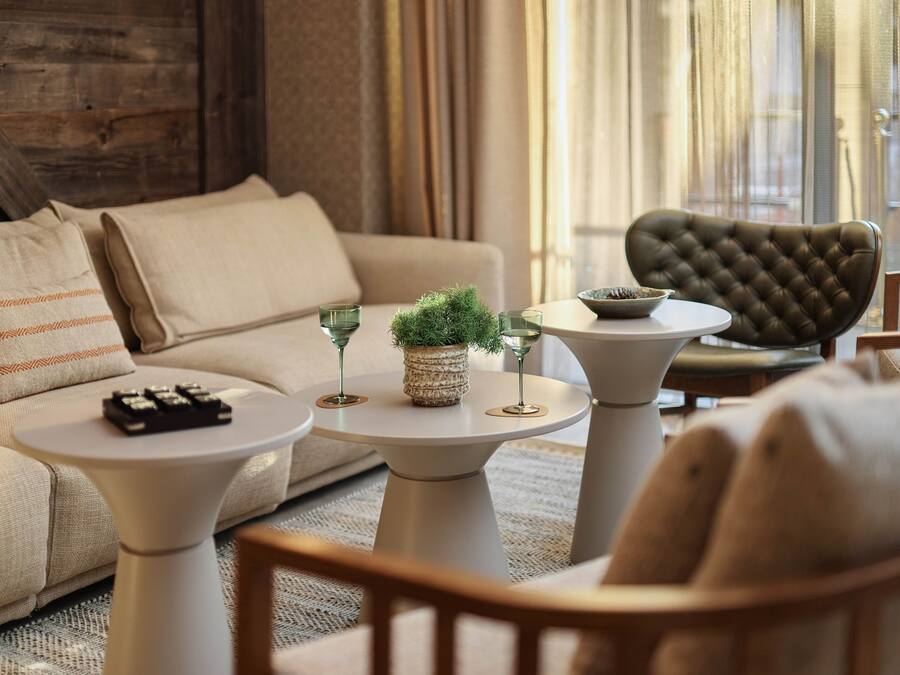 Una sala de estar acogedora con un sofá, dos mesas redondas, una planta decorativa y un sillón capitonado.