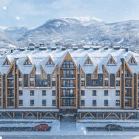 A hotel with a symmetrical facade, multiple balconies, and a snowy mountain backdrop.