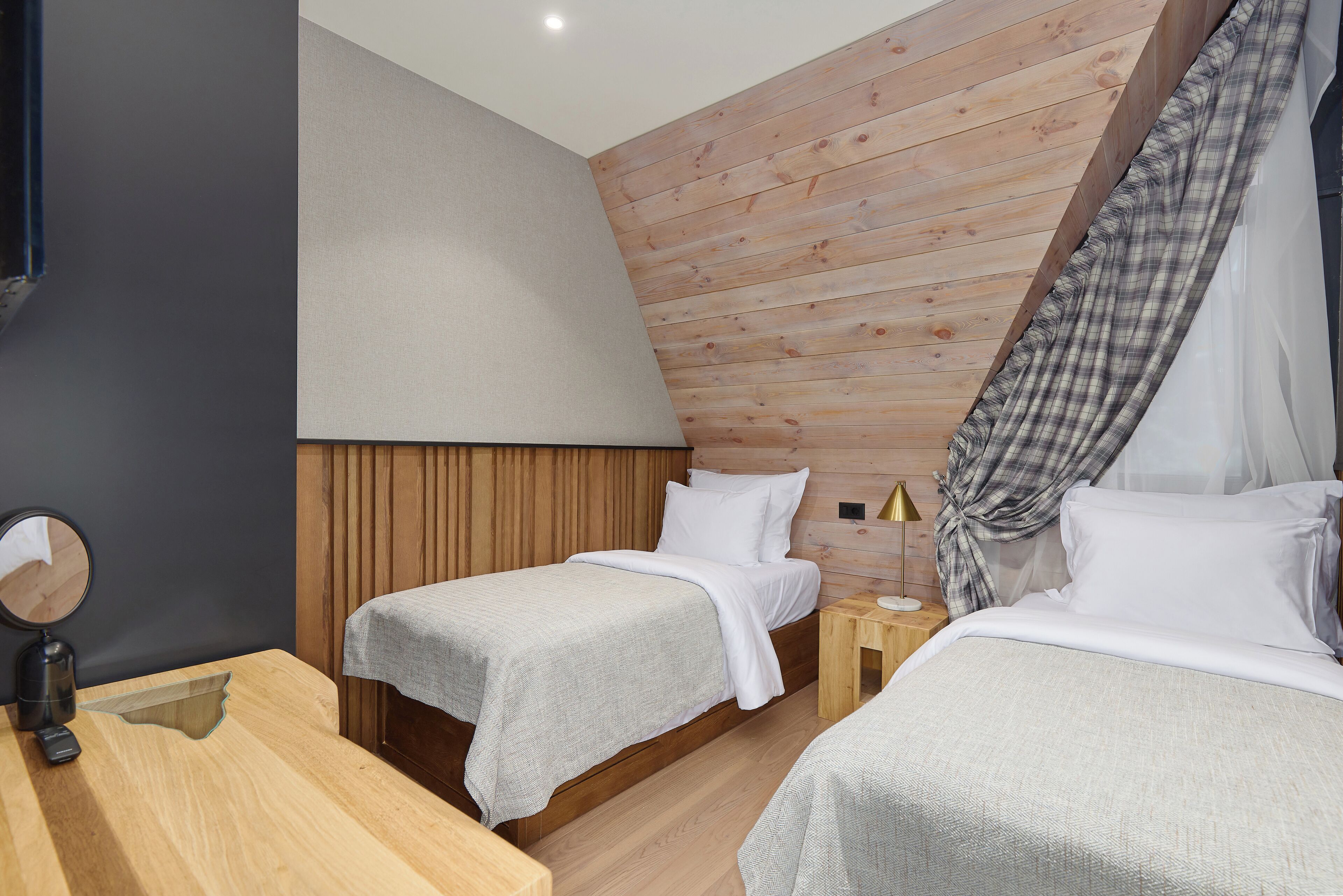 Une chambre moderne avec deux lits, des murs recouverts de panneaux en bois, une petite table de chevet avec une lampe et un miroir sur le côté gauche.