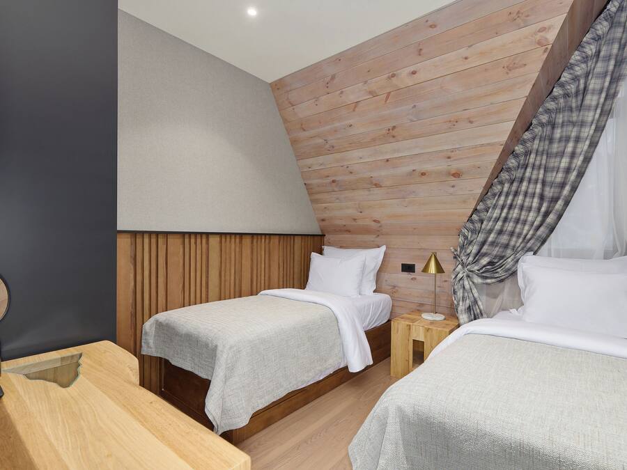 Une chambre moderne avec deux lits, des murs recouverts de panneaux en bois, une petite table de chevet avec une lampe et un miroir sur le côté gauche.