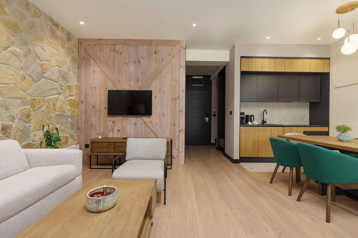 A modern living room with a stone wall, a flat-screen TV, a sofa, a coffee table, and a dining area with chairs.