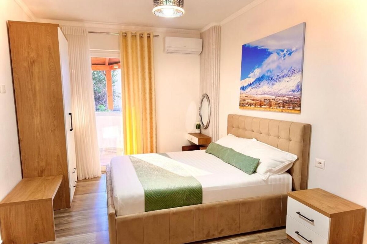 A bedroom with a bed, bedside tables, a mirror, and a painting on the wall.