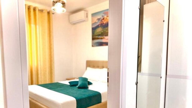 Un dormitorio con una cama, una manta verde, suelo de madera, un cuadro en la pared y una puerta blanca.