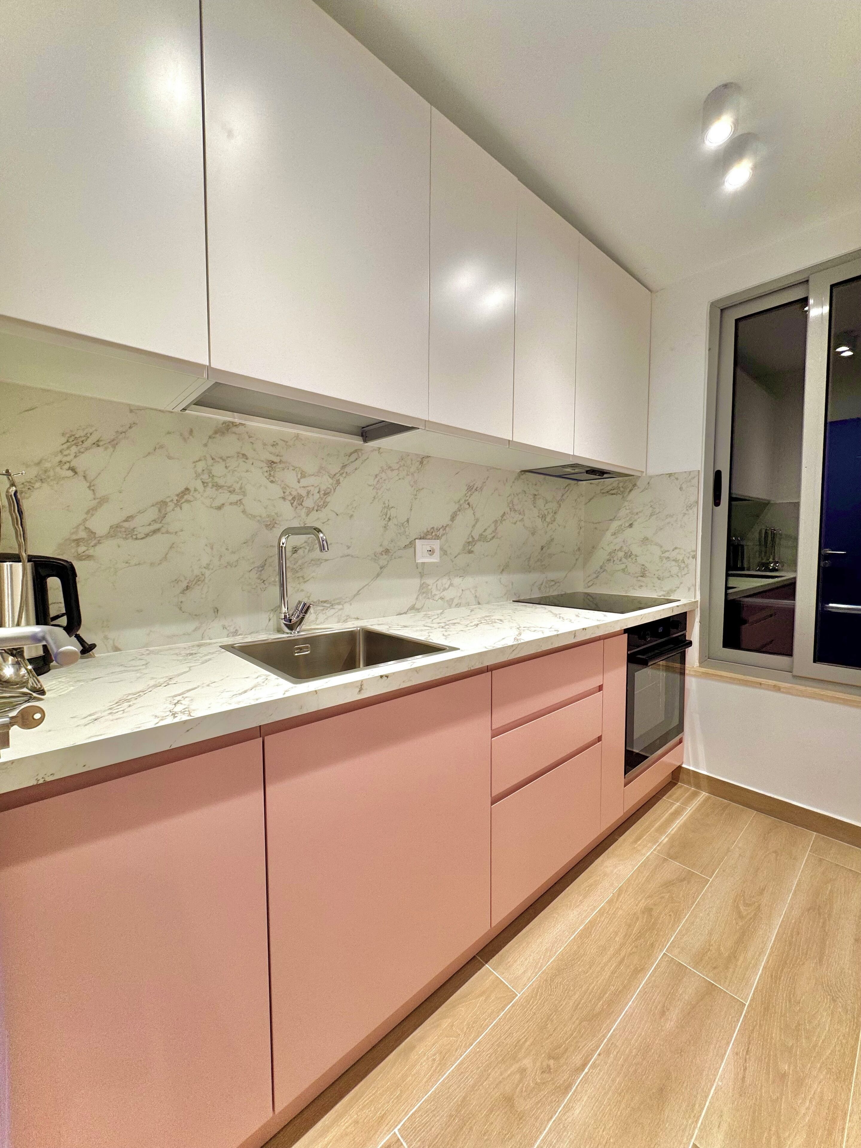 Eine moderne Küche mit weißer Marmor-Spritzschutzleiste, rosa Schränken und einer doppelten Spüle.