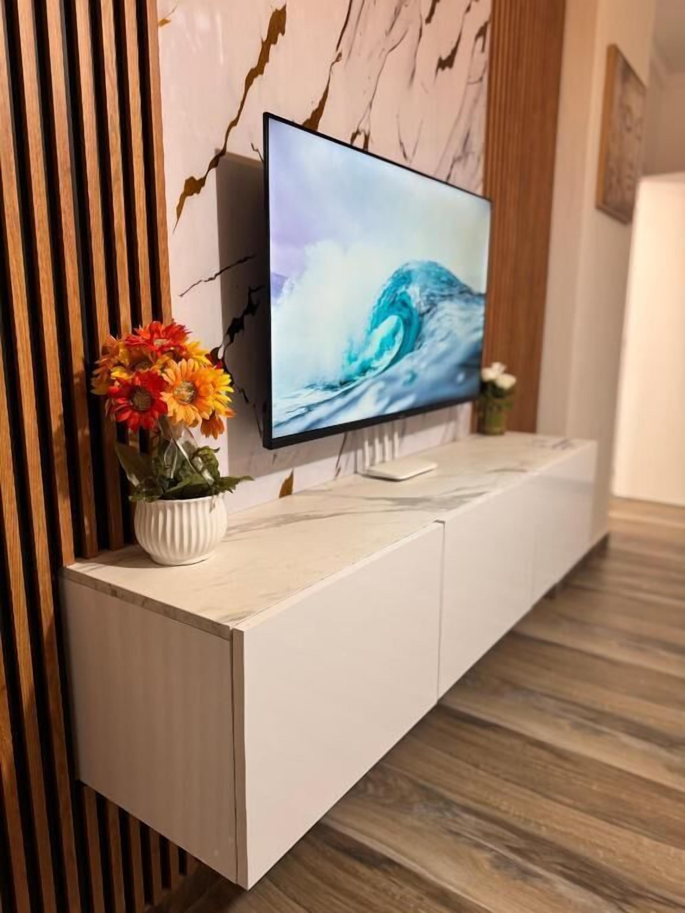 Een flatscreen televisie bevestigd aan een wit kastje, met een marmerachtige wand erachter.