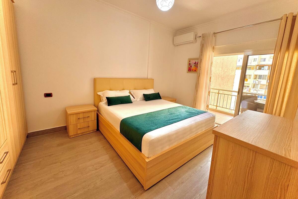 Un dormitorio con una cama de madera, una mesita de noche, un armario y un balcón con vistas a la ciudad.