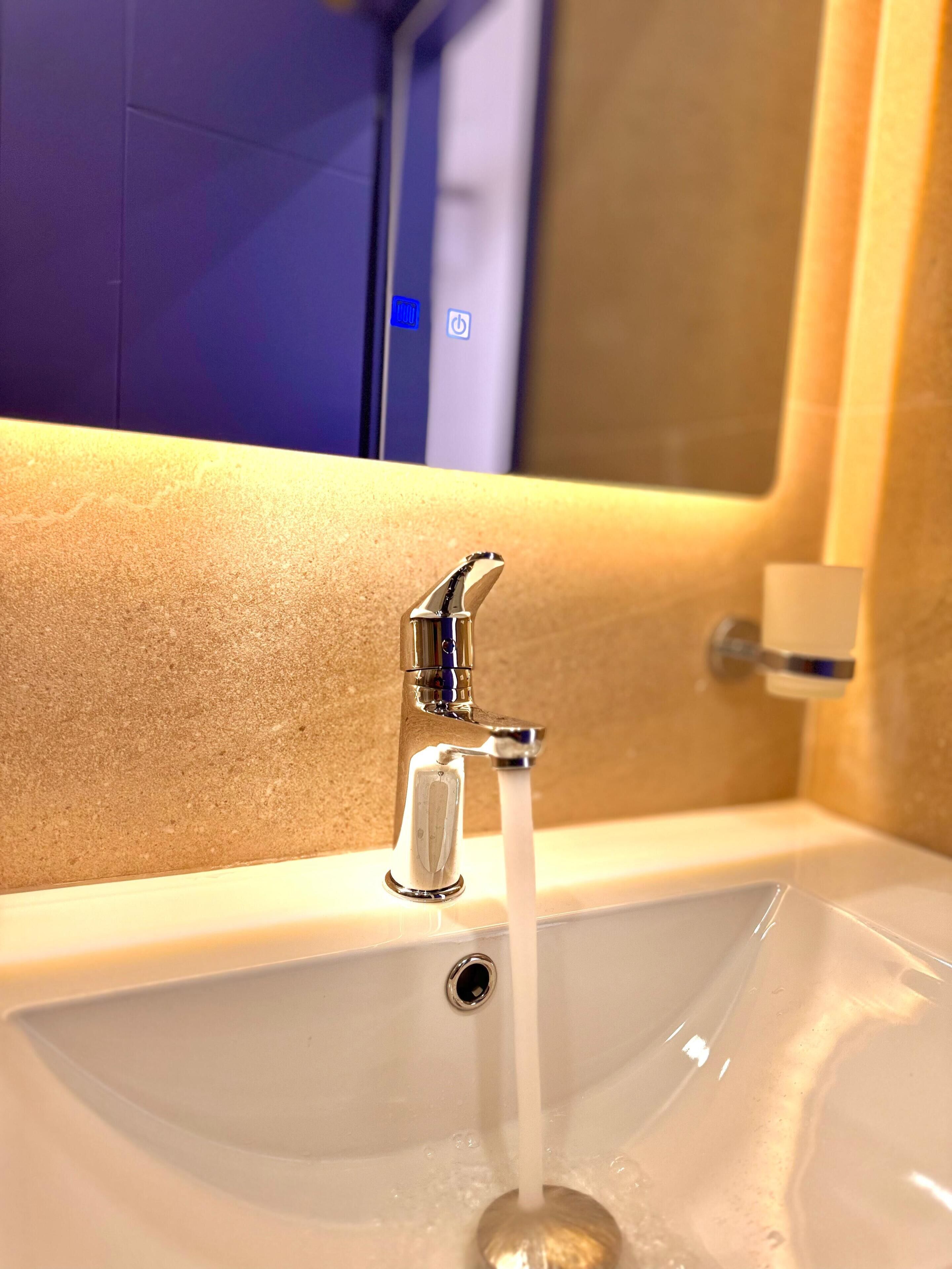 Un lavabo avec eau courante, un miroir et un distributeur de savon.