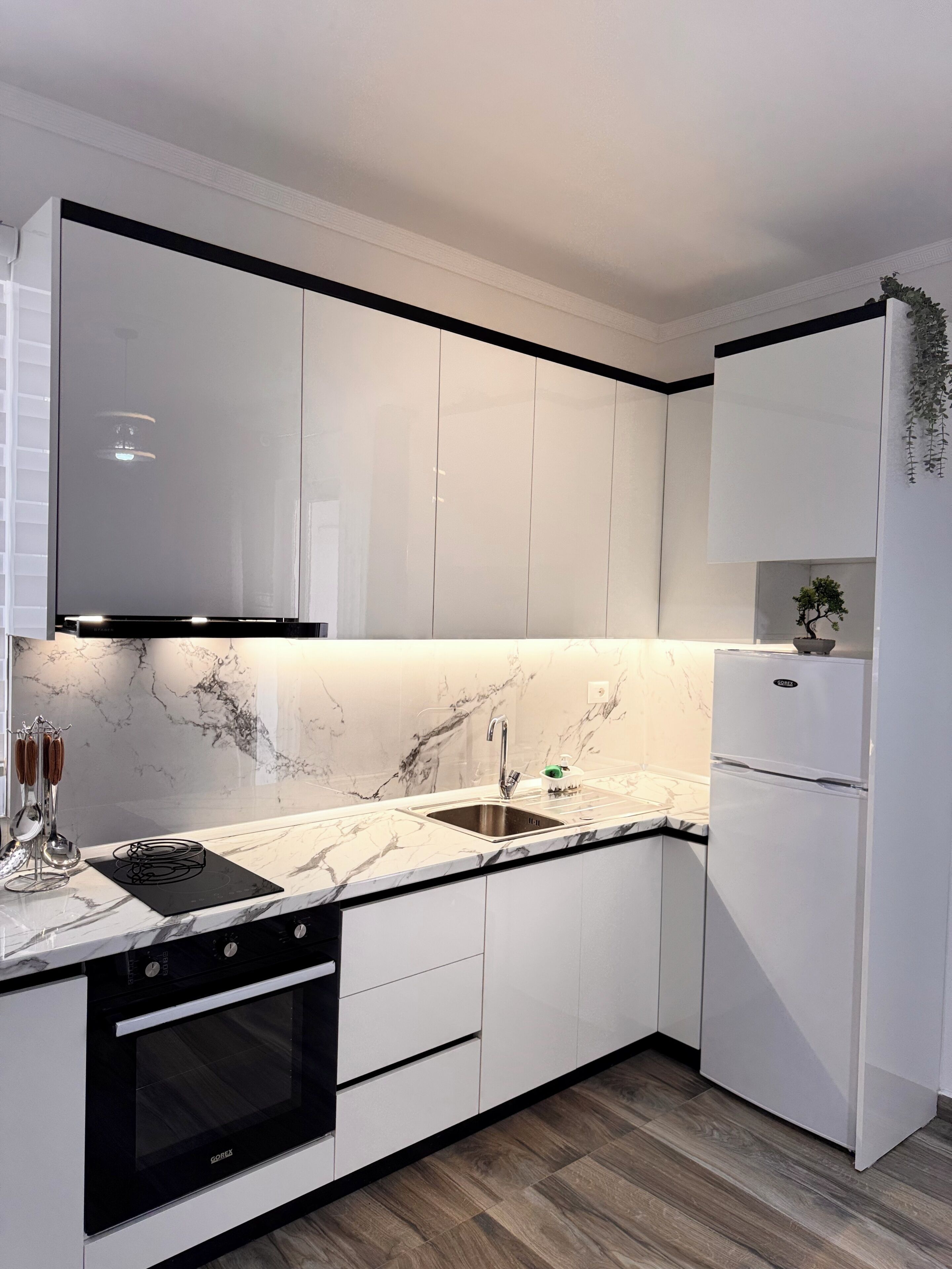 A modern kitchen with white cabinetry, a black countertop, a built-in oven, and a stainless steel sink.