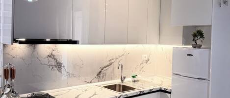 A modern kitchen with white cabinetry, a black countertop, a built-in oven, and a stainless steel sink.