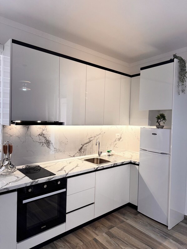 Una cucina moderna con mobili bianchi, un piano di lavoro nero, forno integrato e lavello in acciaio inossidabile.