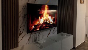 Un soggiorno moderno con una TV a schermo piatto montata su una parete in marmo, un mobile in legno sottostante e un pavimento in legno scuro.