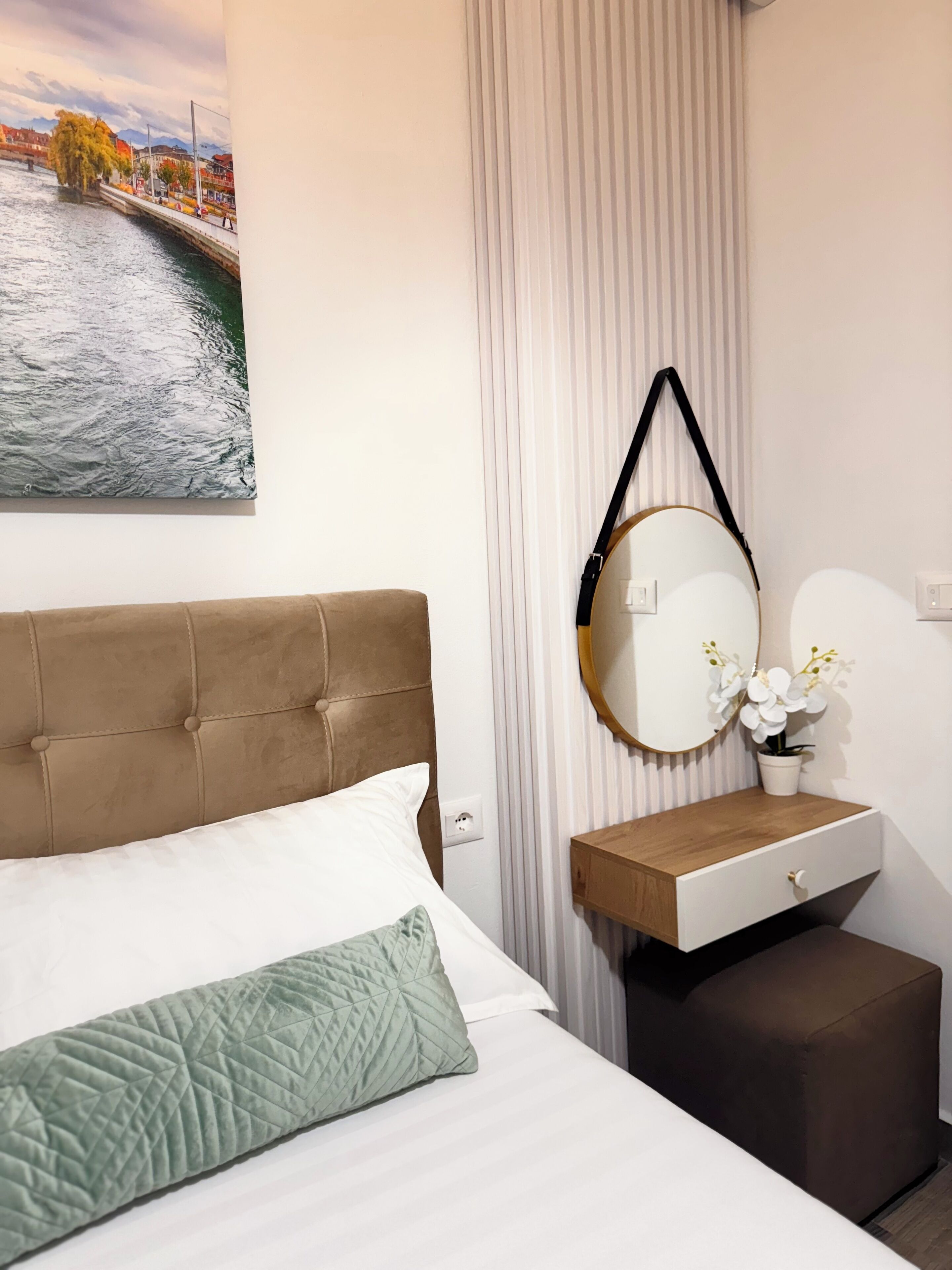 A bedroom with a bed, a bedside table with a mirror, a small wooden nightstand, and a potted orchid.