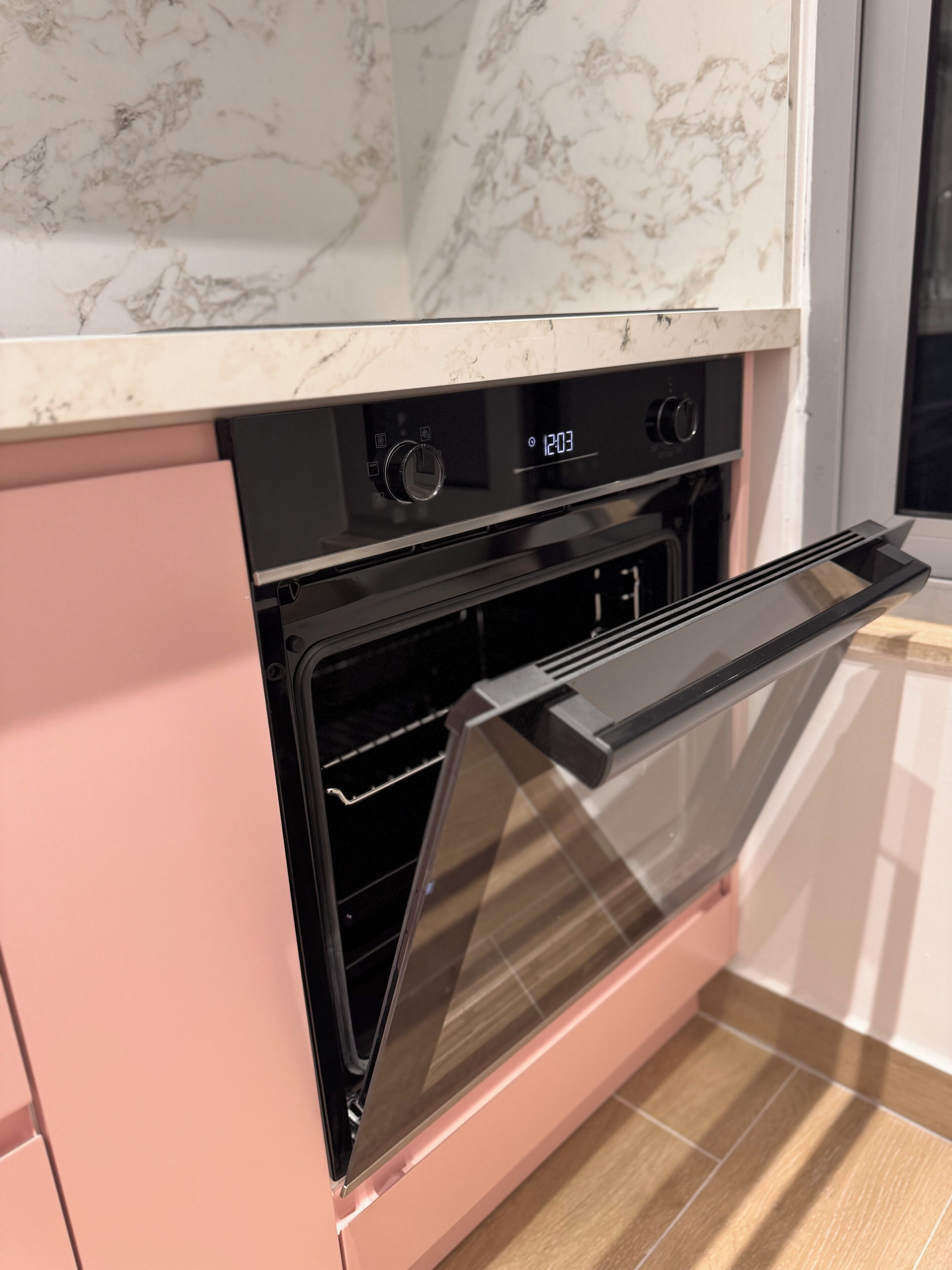 A kitchen with a built-in oven, a pink cabinet, and a marble countertop.