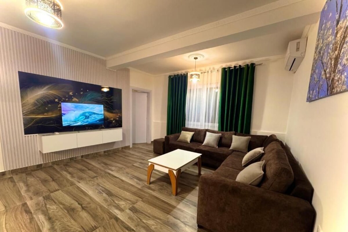 A living room with a flat-screen TV mounted on a white wall, a brown sofa, a white coffee table, and a wooden floor.