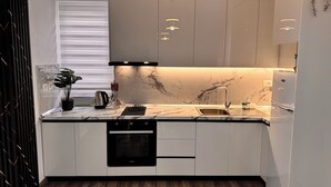 Una cucina moderna con mobili bianchi, una parete rivestita in marmo, forno integrato e lavastoviglie.