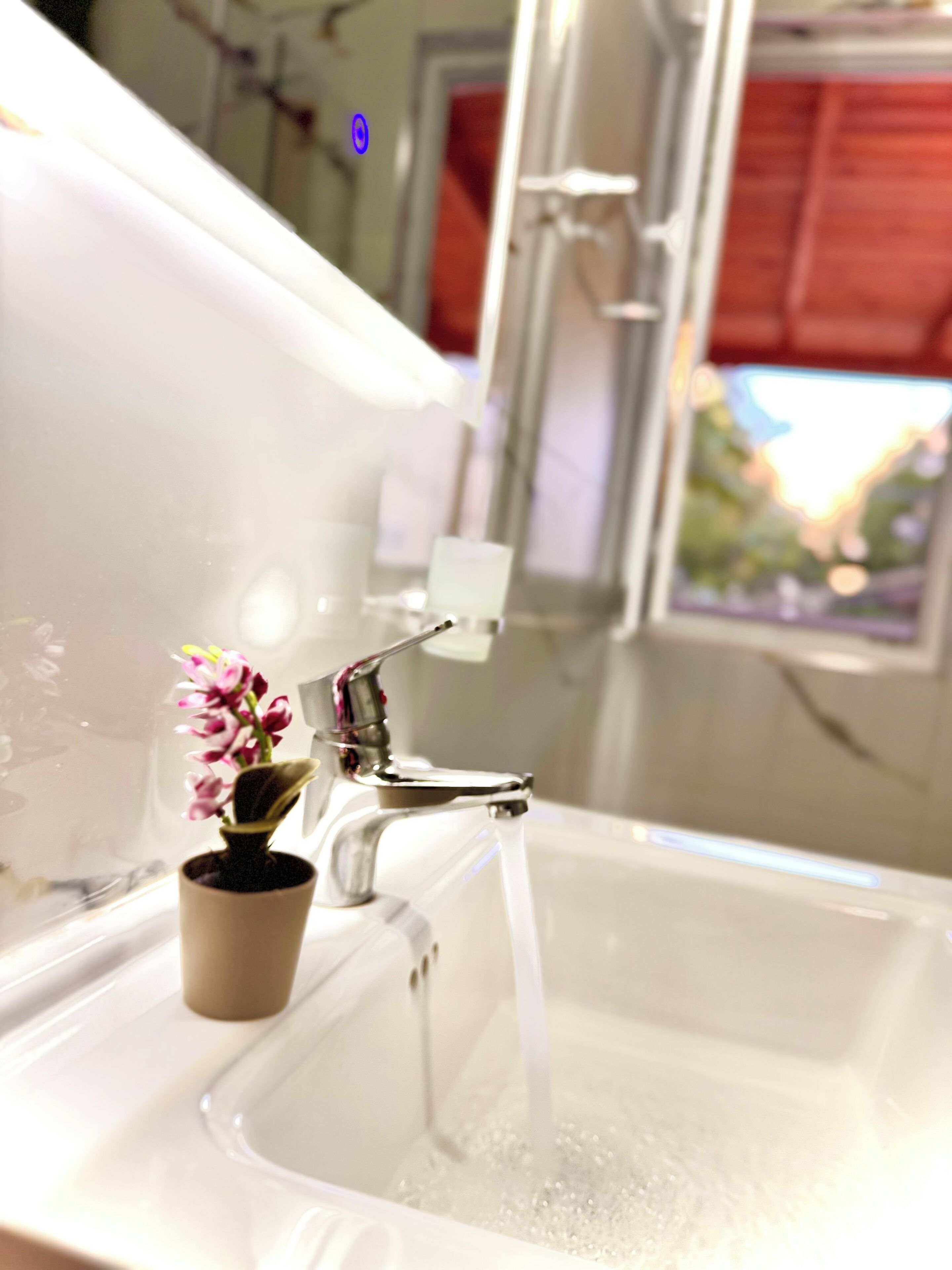 A bathroom sink with running water, a small potted plant, and a window with a view.