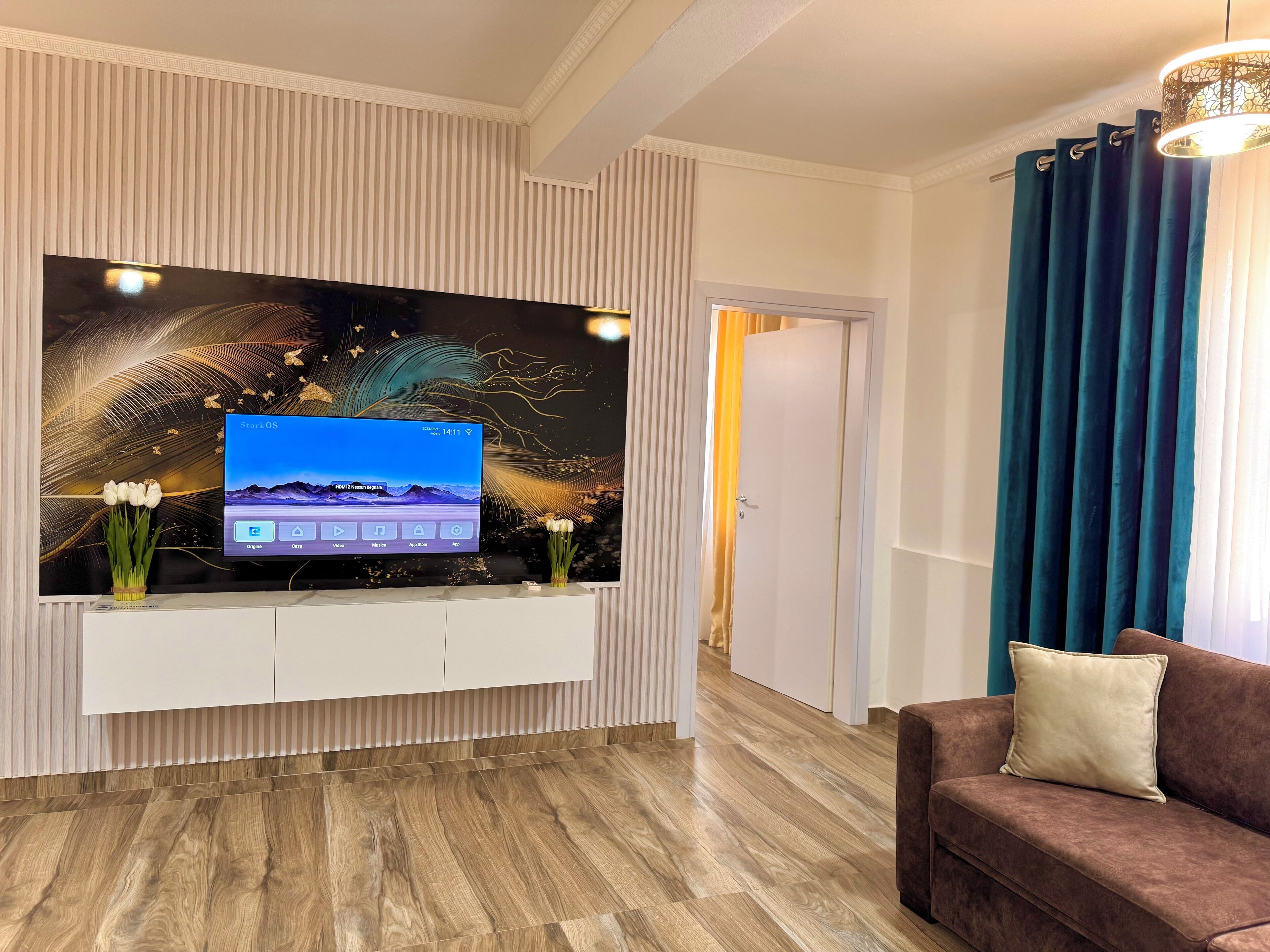 Un salon moderne avec un téléviseur fixé au mur, un plancher en bois, un canapé marron et un panneau décoratif mural.