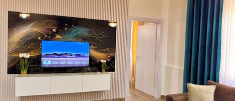Un salon moderne avec un téléviseur fixé au mur, un plancher en bois, un canapé marron et un panneau décoratif mural.