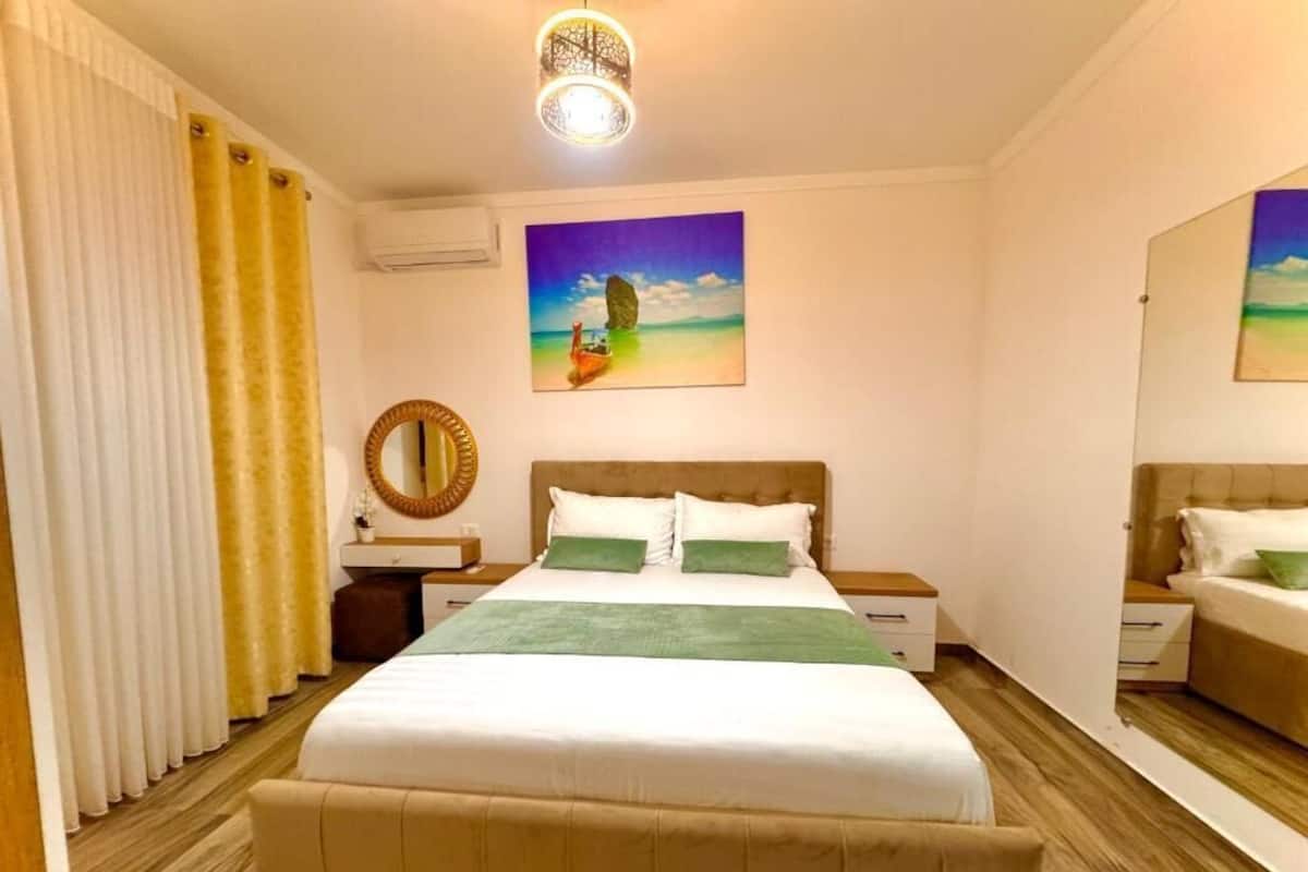 Habitación de hotel con una cama grande, una mesita de noche, un espejo y un cuadro en la pared.