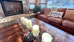 A cozy living room with a stone fireplace, a leather sofa, and a coffee table with candles. - Eagles Nest • Mtn Views • Dog-Friendly • Ev Charger • Ski/Hike (Silverthorne)