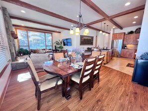 A spacious dining area with a wooden table and chairs, a kitchen with wooden cabinets, and a living room with a sofa and a TV.