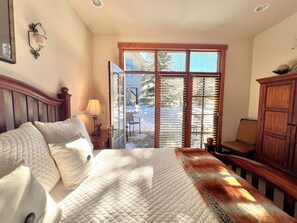 A bedroom with a bed, a nightstand, a lamp, a wooden cabinet, and a view of a snowy outdoor area through a glass door.