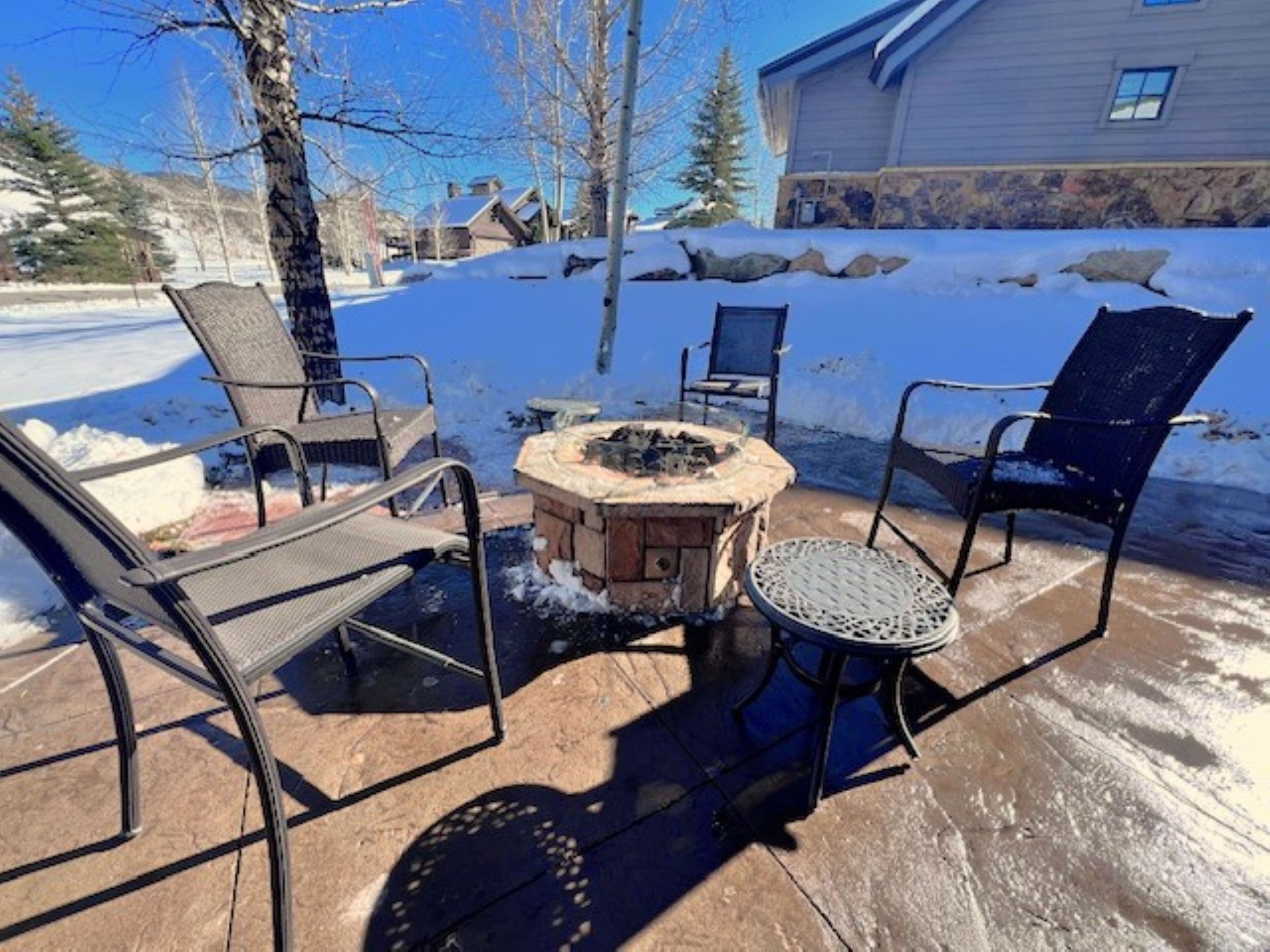 An outdoor seating area with a stone fire pit and metal chairs.