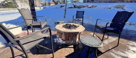 An outdoor seating area with a stone fire pit and metal chairs.