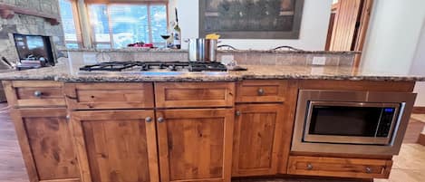 Una cocina con encimera de granito, armarios de madera, horno empotrado y chimenea de piedra.