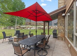 An outdoor patio with a table and chairs, a red umbrella, and a stone wall in the background.